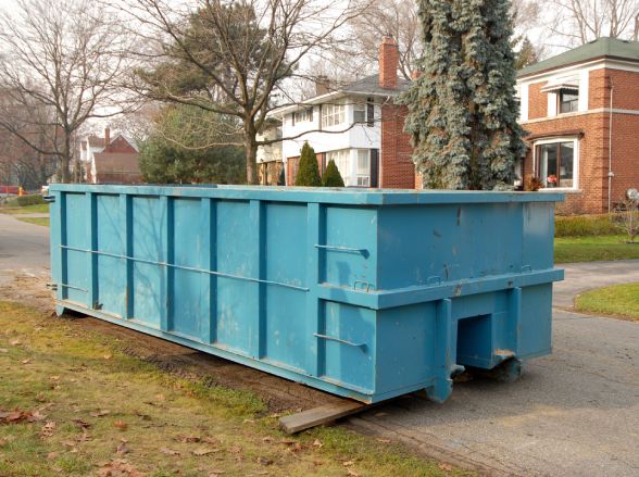 Bluish green dumpster in front of a brick house