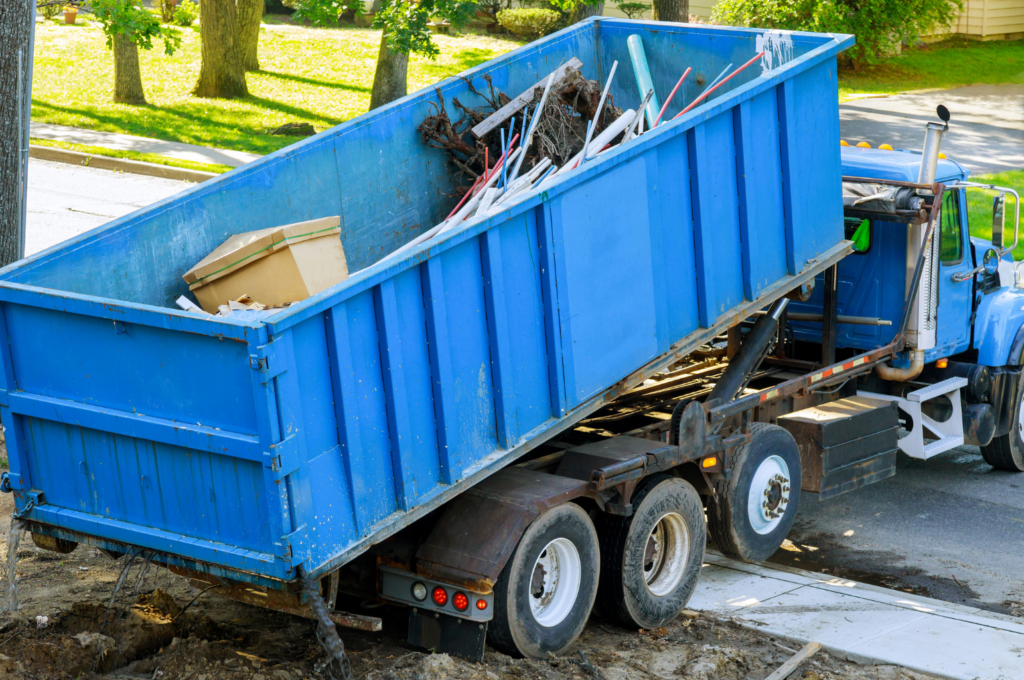 A large blue roll-off dumpster being unloaded from a truck on a residential street.
