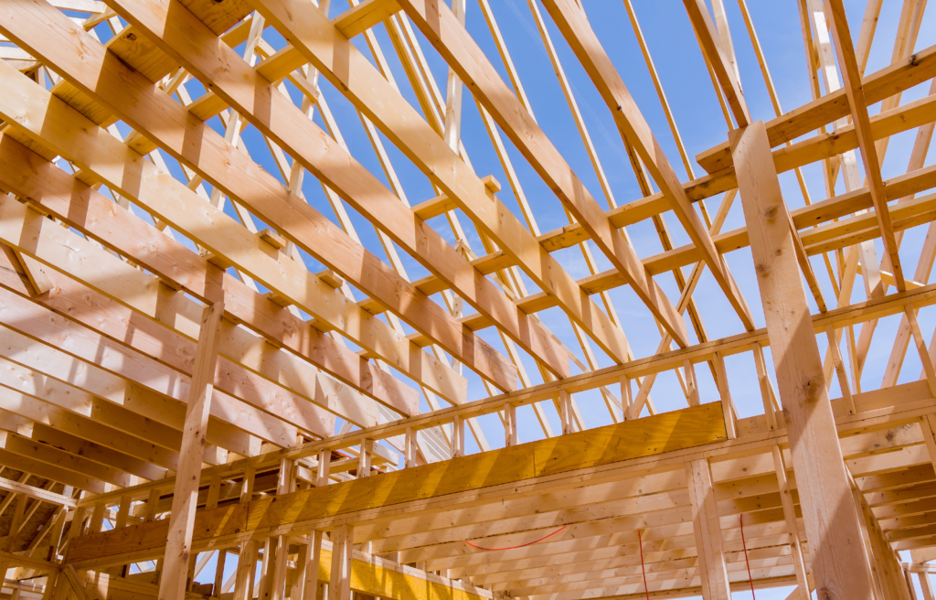Wooden beams form the structure of the roof of a building with the blue sky in the background.