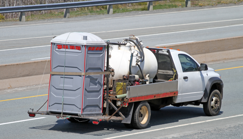 A truck transporting a portable toilet and sanitation equipment on a highway.